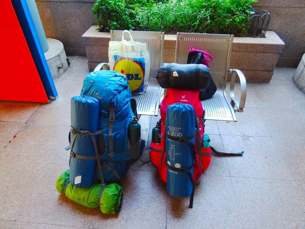 due zaini da trekking rosso e blu appoggiati a due sedie di metallo in una stazione, alla fine di un itinerario interrail in centro europa